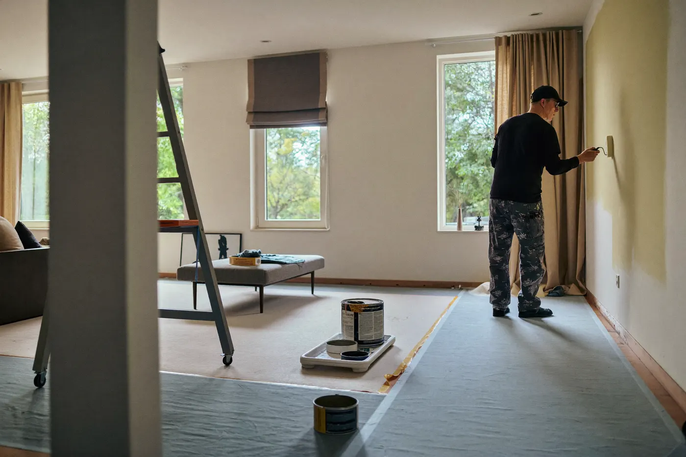 Schilder werkt zorgvuldig aan een wand in een afgeplakte woonkamer